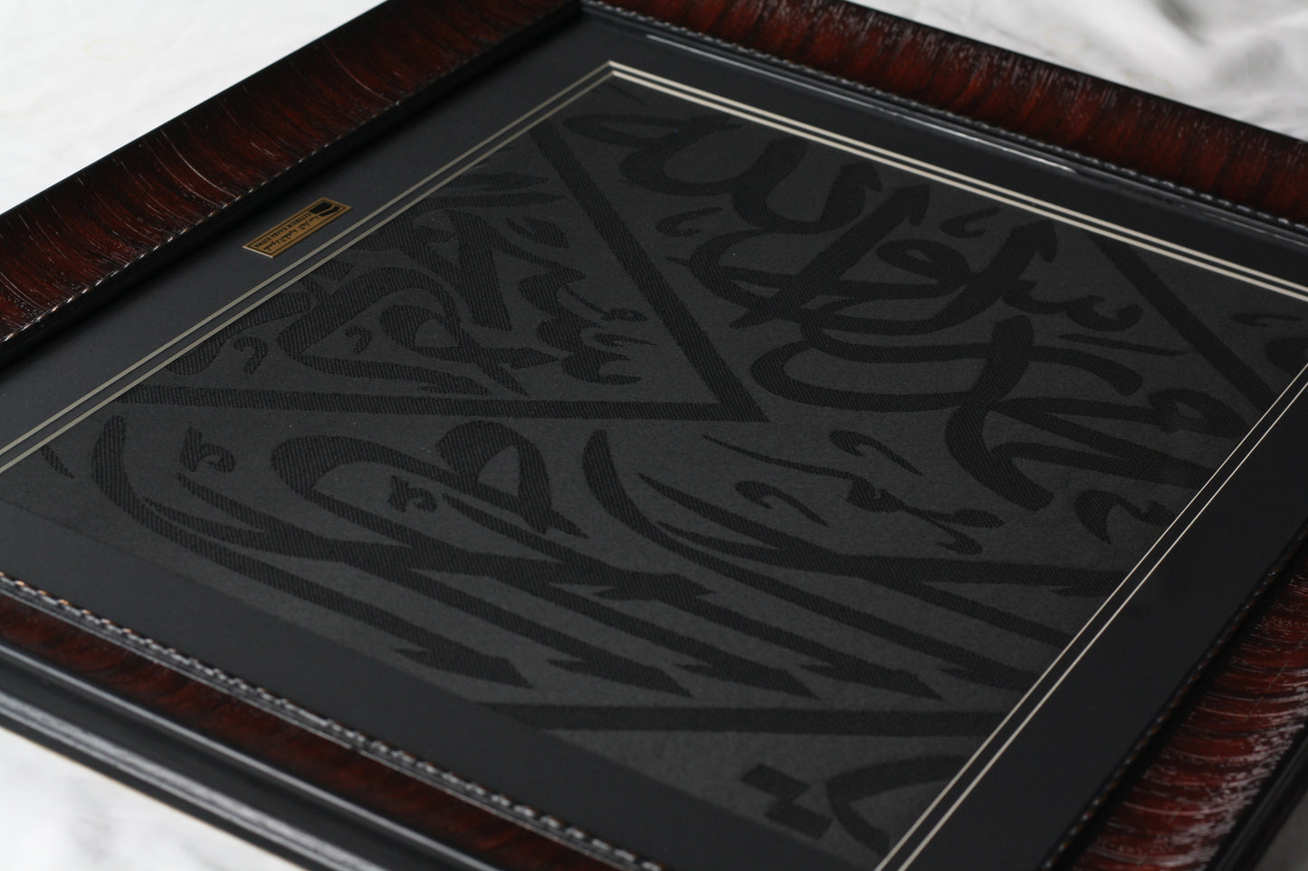 Decorative item with intricate black design on a reflective surface, framed in brown leather.