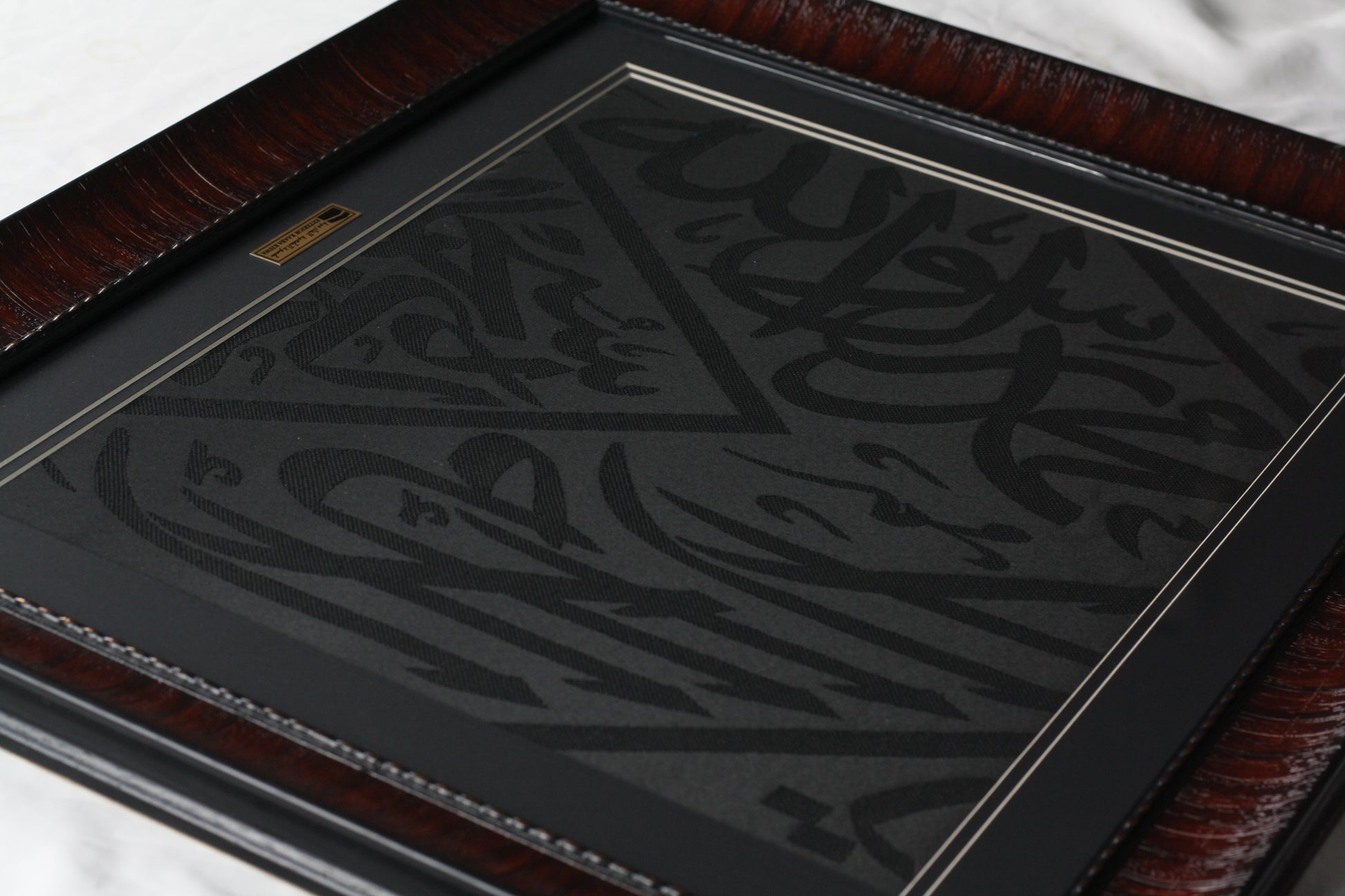 Decorative item with intricate black design on a reflective surface, framed in brown leather.